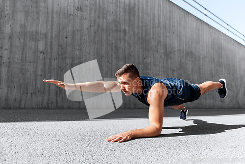 Image of young man doing plank on city street