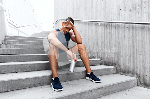 Image of tired sportsman with bottle sitting on stairs