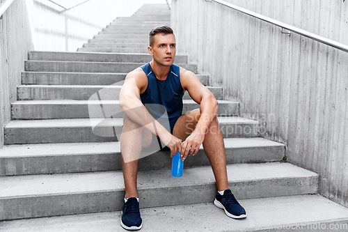 Image of tired sportsman with bottle sitting on stairs