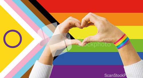 Image of couple showing hand heart over progress pride flag