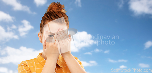 Image of red haired teenage girl looking through fingers