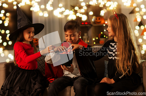 Image of kids in halloween costumes sharing candies at home