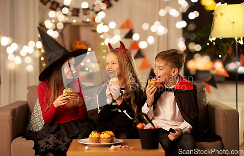 Image of kids in halloween costumes eating cupcakes at home