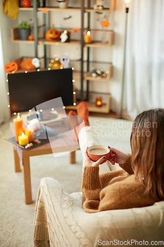 Image of woman watches tv and drinks cocoa on halloween