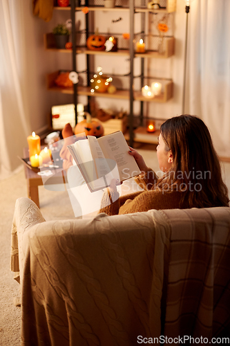 Image of young woman reading book at home on halloween