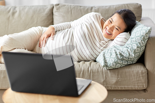 Image of happy pregnant asian woman with laptop at home