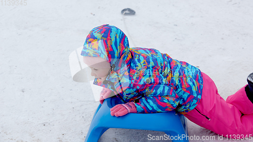 Image of Cheerful girl riding a sled downhill on a snow covered sledge trail in a white sunny winter mountain landscape