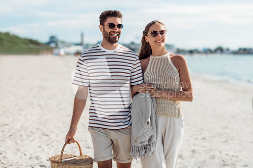 Image of happy couple with picnic basket walking on beach