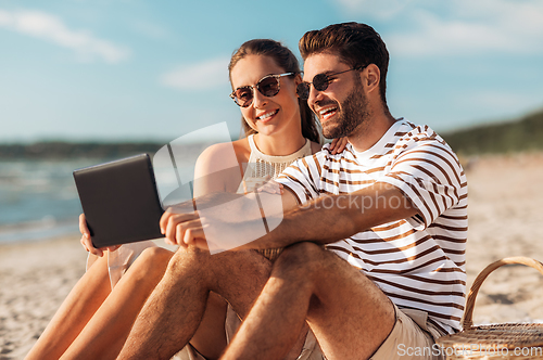 Image of happy couple with tablet pc at picnic on beach