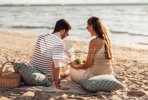 Image of happy couple with food having picnic on beach