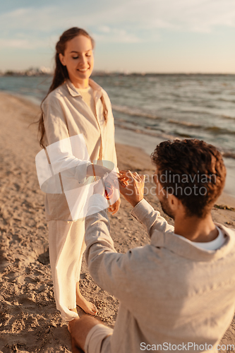 Image of man with ring making proposal to woman on beach