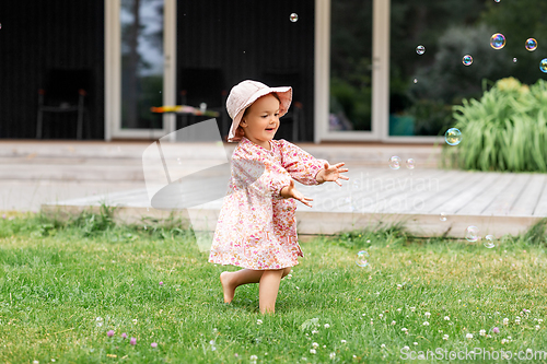 Image of happy baby girl playing with soap bubbles outdoors