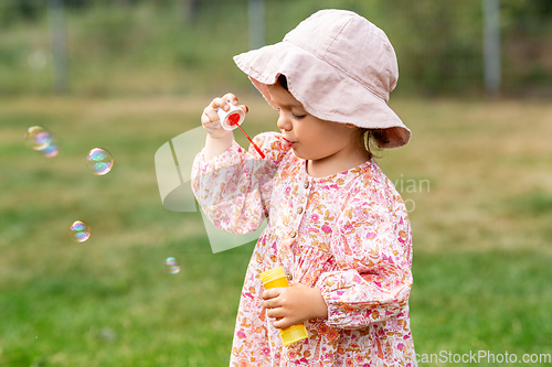 Image of happy baby girl blowing soap bubbles in summer