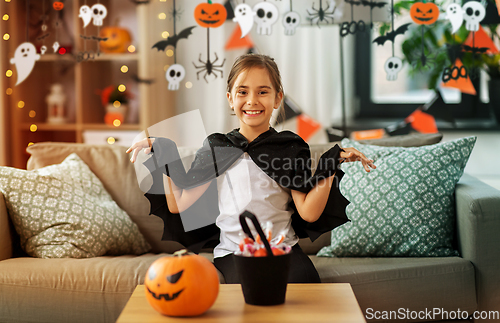 Image of girl in halloween costume with bat cape at home