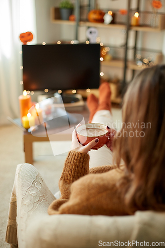 Image of woman watches tv and drinks cocoa on halloween