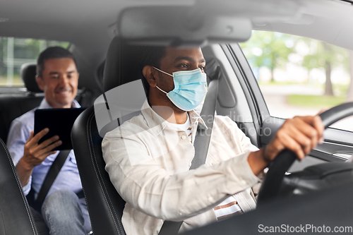 Image of passenger with tablet pc and car driver in mask