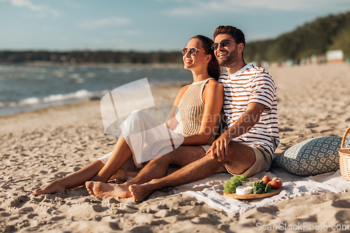 Image of happy couple with food having picnic on beach