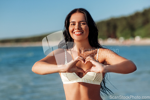 Image of smiling young woman in showing hand heart on beach