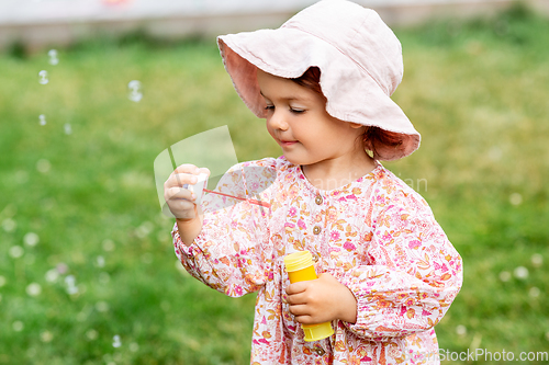 Image of happy baby girl blowing soap bubbles in summer