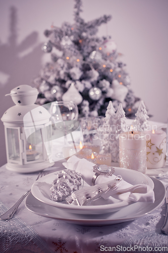 Image of Festive  Christmas table place setting with silverware, candles and decorated Christmas tree