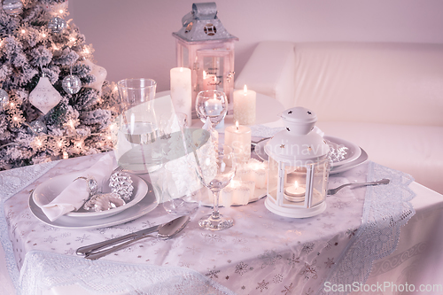 Image of Festive  Christmas table place setting with silverware, candles and decorated Christmas tree