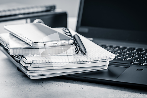 Image of Office table - stack of notebooks, cellphone with laptop