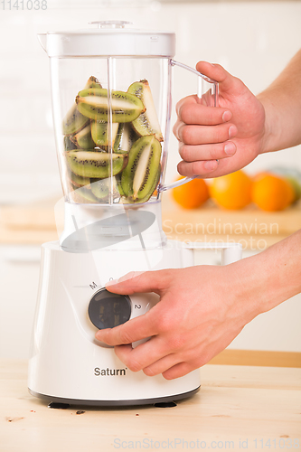 Image of Young man cooking kiwi smoothie in blender