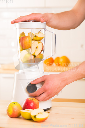 Image of Young man cooking apple smoothie in blender