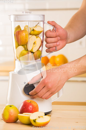 Image of Young man cooking apple smoothie in blender