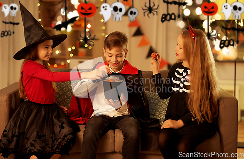 Image of kids in halloween costumes share candies at home