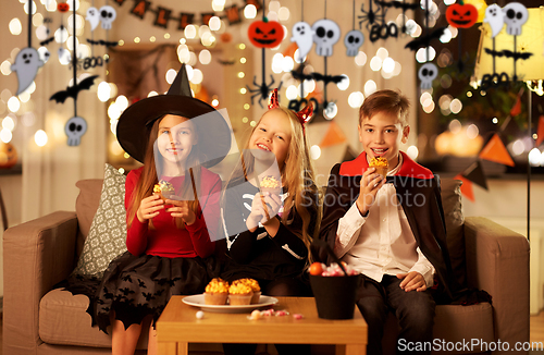 Image of kids in halloween costumes eating cupcakes at home