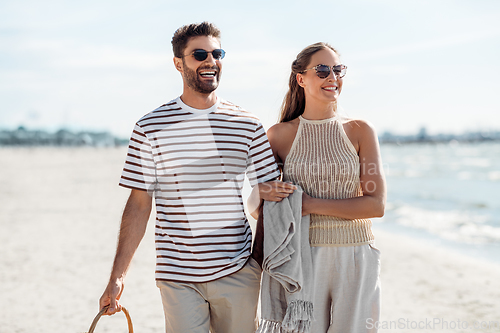 Image of happy couple with blanket walking along beach