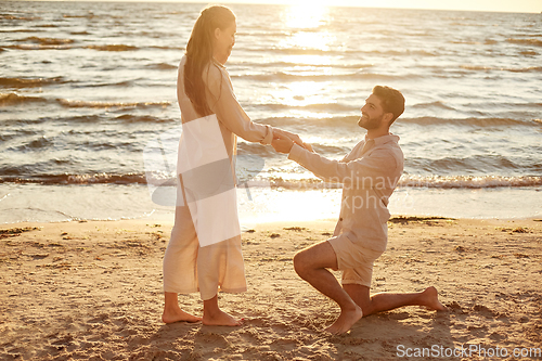 Image of man with ring making proposal to woman on beach