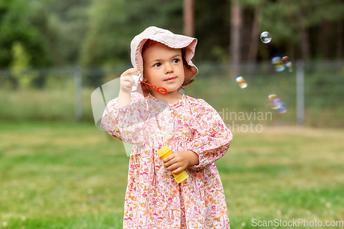 Image of happy baby girl blowing soap bubbles in summer