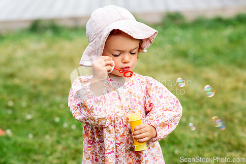 Image of happy baby girl blowing soap bubbles in summer