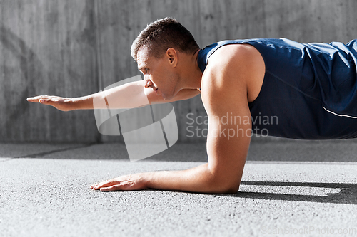 Image of young man doing plank on city street