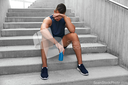 Image of tired sportsman with bottle sitting on stairs