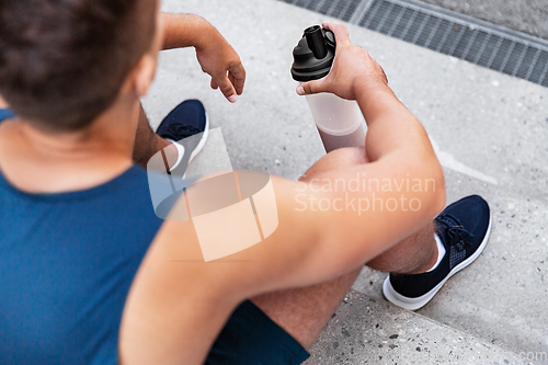 Image of sportsman with shake in bottle sitting on stairs