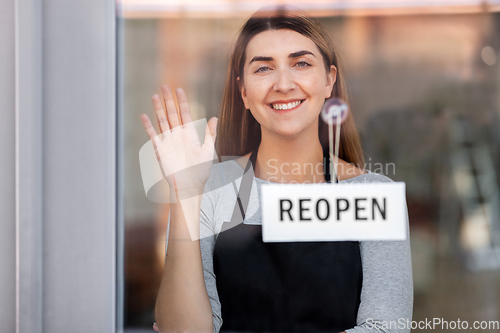 Image of happy woman hanging reopen banner to door glass