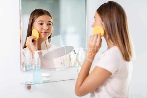 Image of teenage girl cleaning face with sponge at bathroom