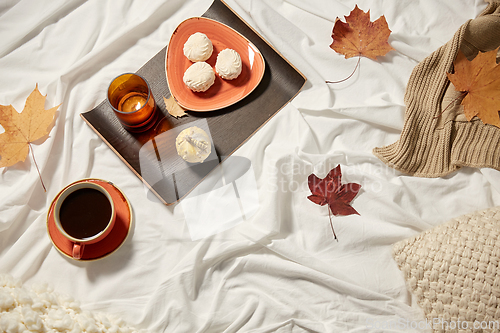 Image of cup of coffee, autumn leaves and candle in bed