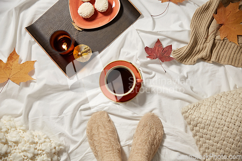 Image of cup of coffee, autumn leaves and candle in bed