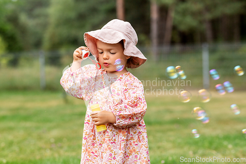 Image of happy baby girl blowing soap bubbles in summer