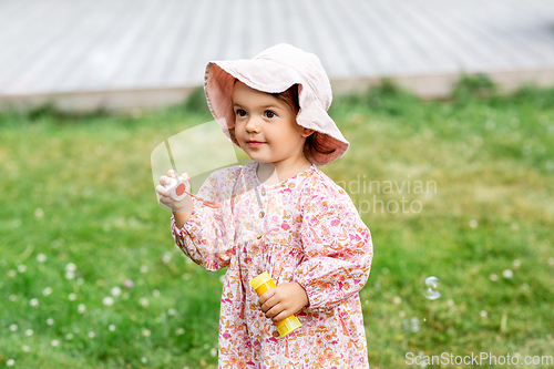 Image of happy baby girl blowing soap bubbles in summer