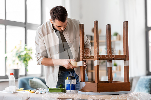 Image of man sticking adhesive tape to table for repainting