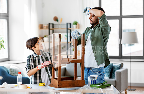 Image of tired father and son sanding old table with sponge