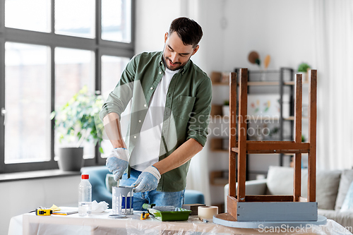 Image of man stirring can with grey color paint at home