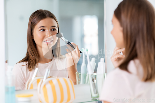 Image of teenage girl applying blush to face at bathroom