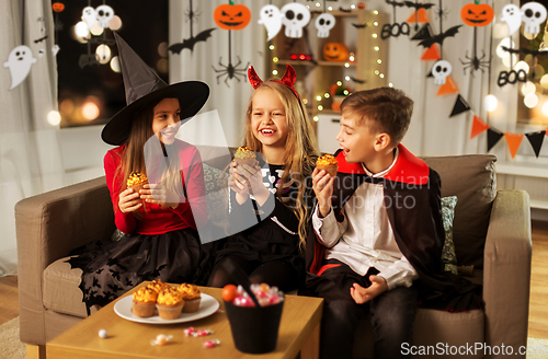 Image of kids in halloween costumes eating cupcakes at home