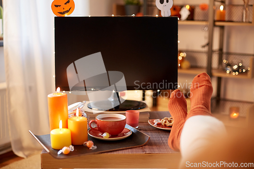 Image of young woman watching tv at home on halloween